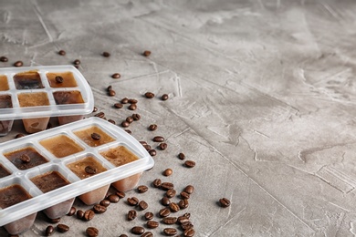 Photo of Ice cubes in trays and coffee beans on grey table. Space for text