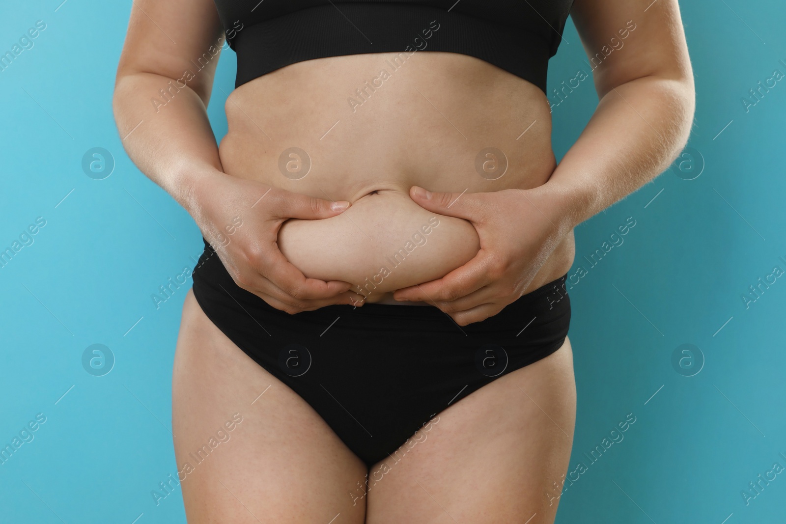 Photo of Woman touching belly fat on light blue background, closeup. Overweight problem