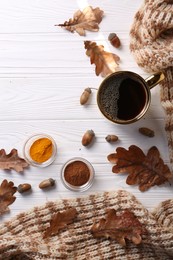 Cup of hot drink, spices, leaves and knitted scarf on white wooden table, flat lay. Cozy autumn atmosphere