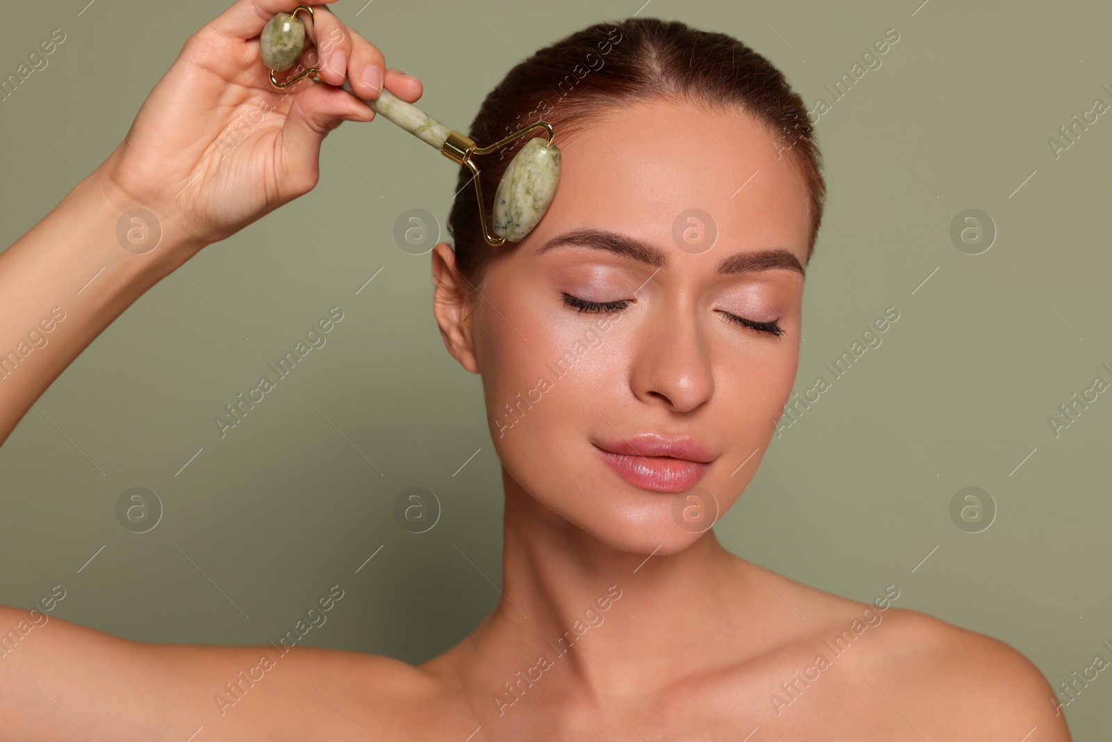 Photo of Young woman massaging her face with jade roller on green background