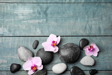 Photo of Stones with orchid flowers and space for text on blue wooden background, flat lay. Zen lifestyle