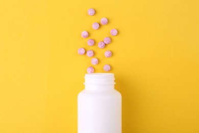 Photo of Bottle and vitamin pills on yellow background, top view