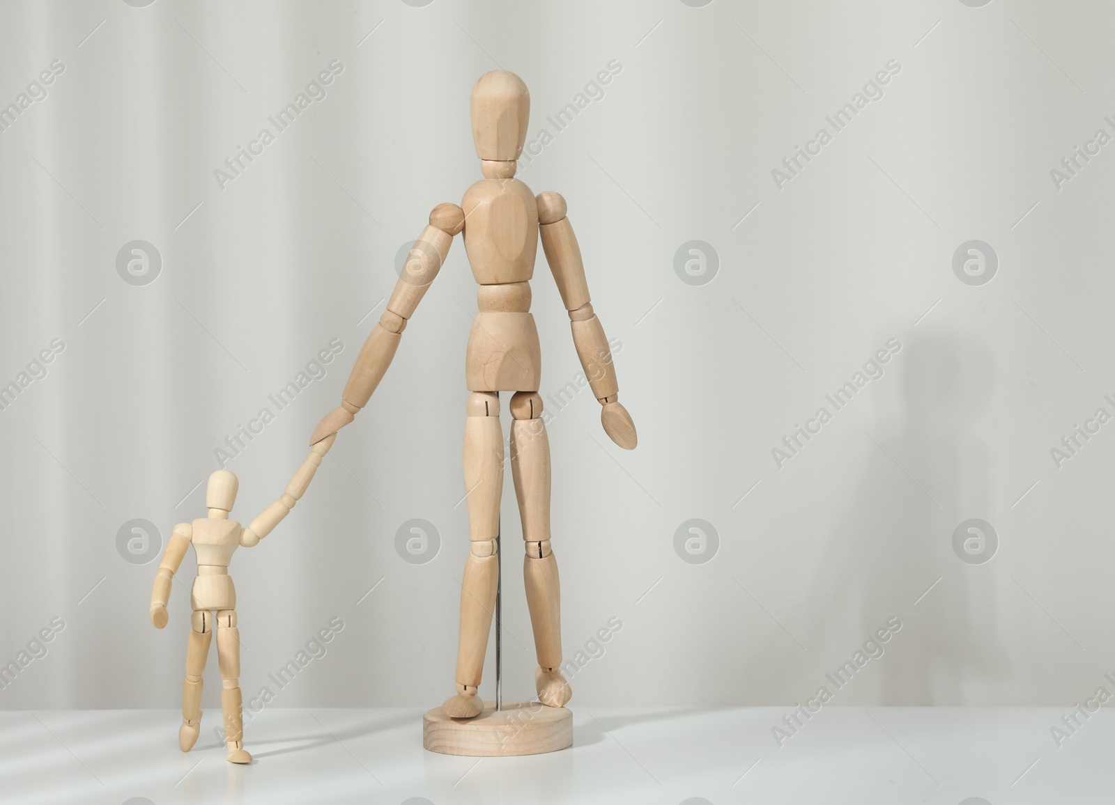 Photo of Wooden mannequins of parent with child on white table against light background, space for text. Family Day