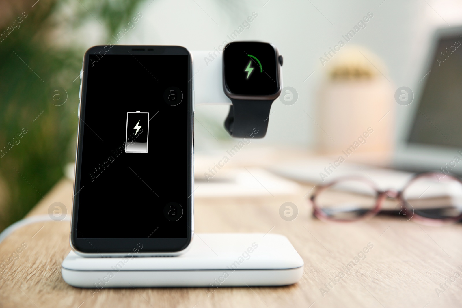 Photo of Mobile phone and smartwatch with wireless charger on wooden table. Modern workplace accessory