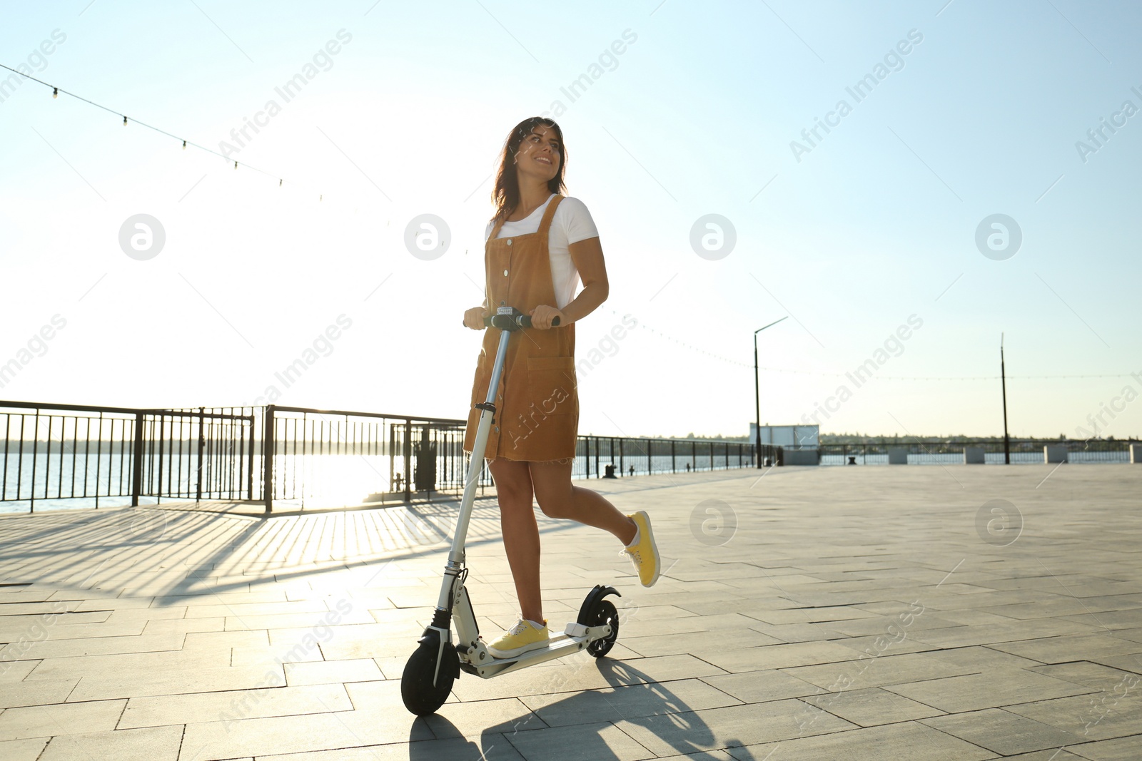 Photo of Young woman riding kick scooter along city street