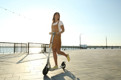 Young woman riding kick scooter along city street