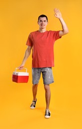 Man with red cool box walking and greeting someone on orange background