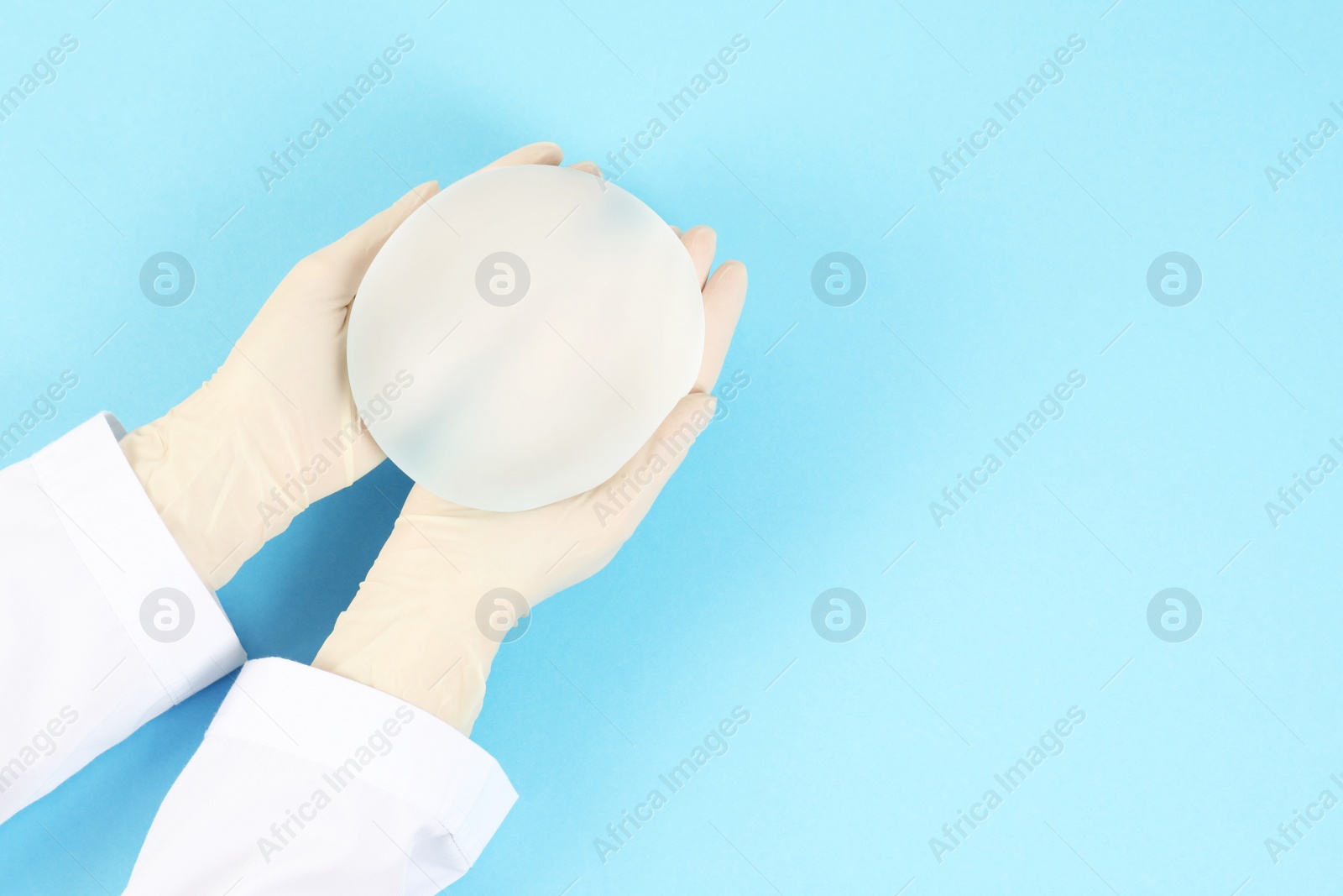 Photo of Doctor holding silicone implant for breast augmentation on color background, top view with space for text. Cosmetic surgery