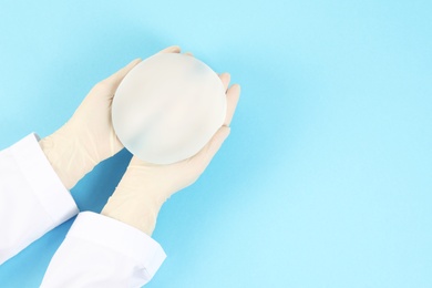 Doctor holding silicone implant for breast augmentation on color background, top view with space for text. Cosmetic surgery