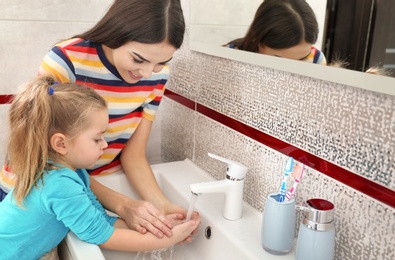 Happy mother and daughter washing hands in bathroom at home