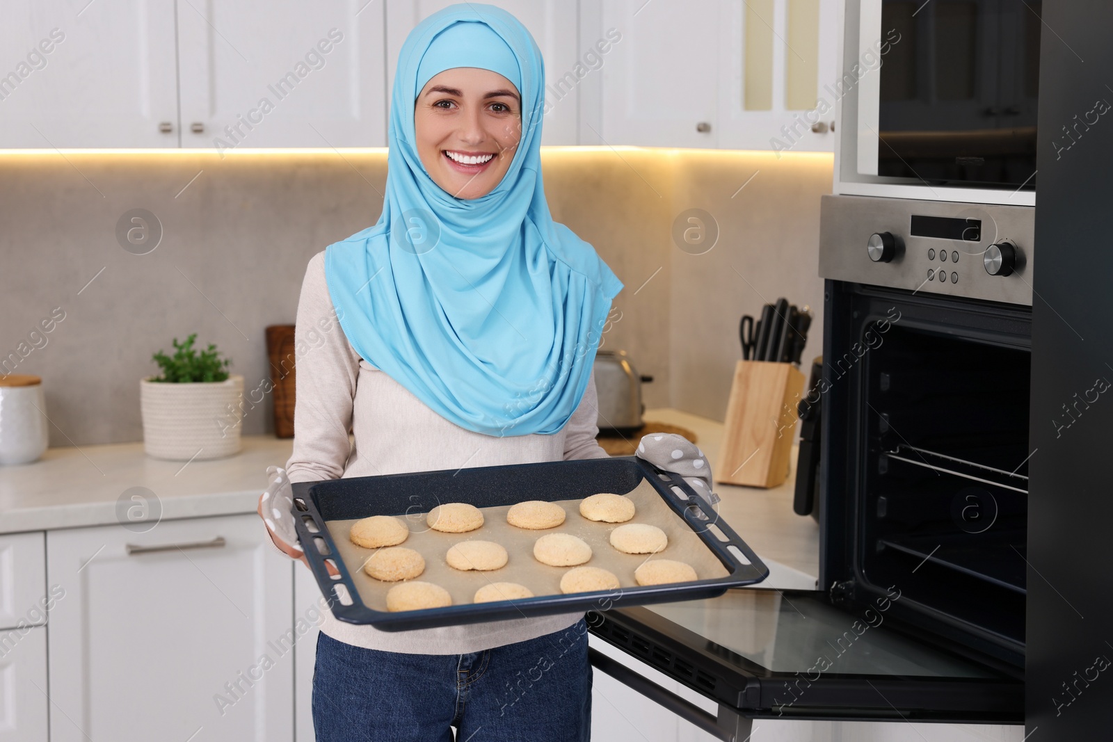 Photo of Muslim woman holding tray with cookies in kitchen