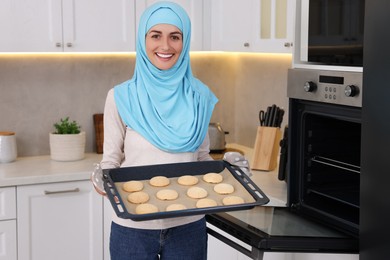 Muslim woman holding tray with cookies in kitchen