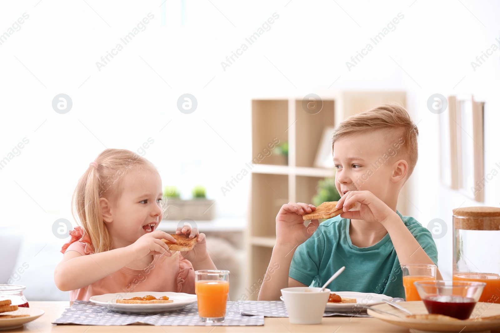 Photo of Adorable little children eating tasty toasted bread with jam at table