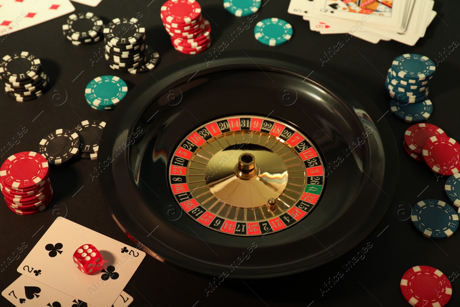 Photo of Roulette wheel, playing cards and chips on table, closeup. Casino game