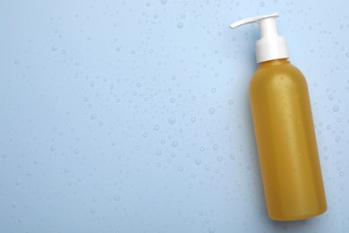 Photo of Wet bottle of face cleansing product on light blue background, top view. Space for text