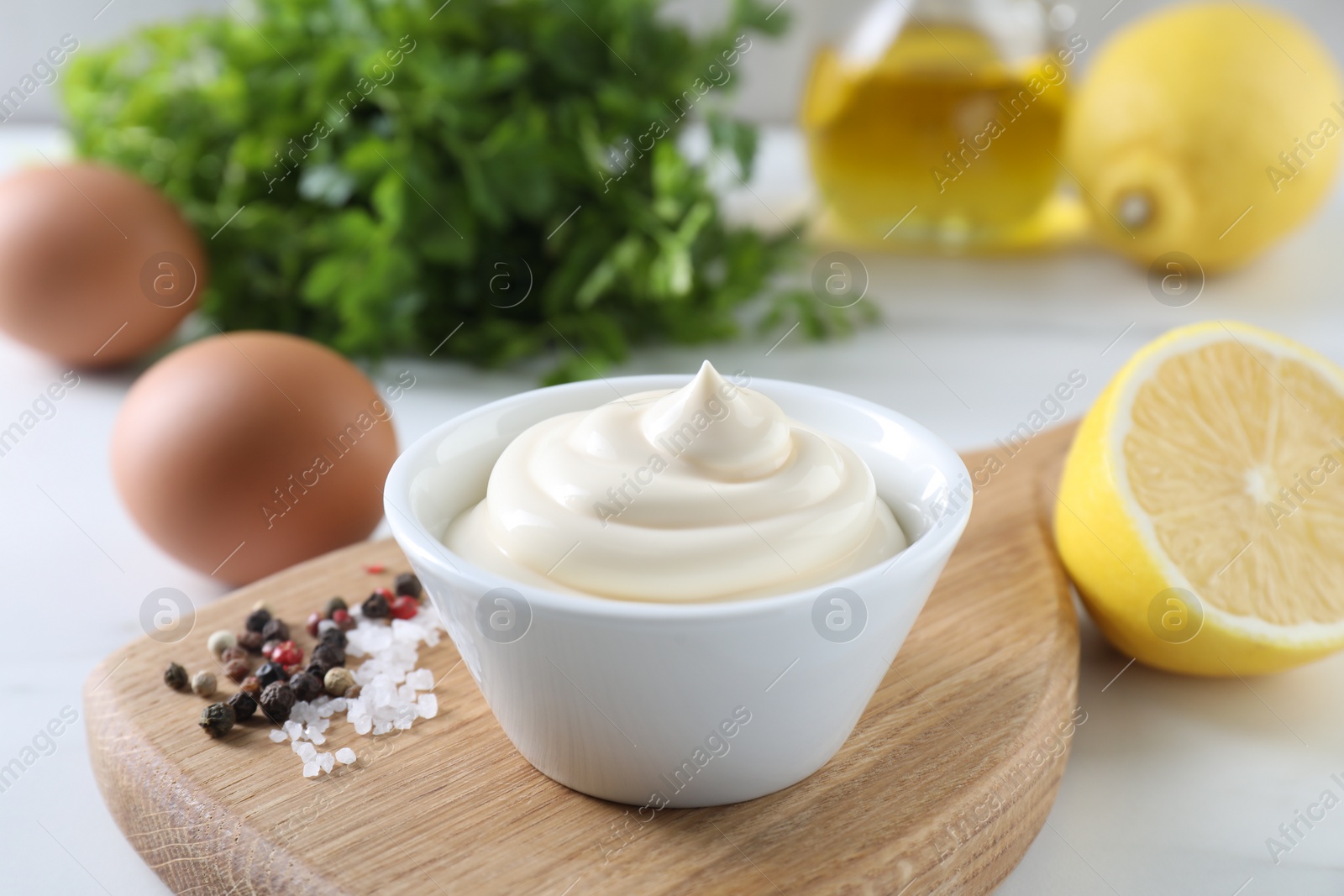 Photo of Tasty mayonnaise sauce in bowl, spices and ingredients on white table, closeup