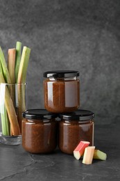 Photo of Jars of tasty rhubarb jam and stalks on grey table