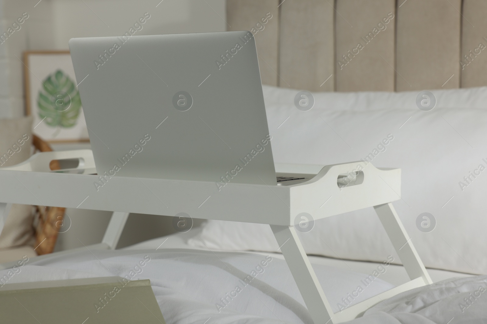 Photo of White tray with modern laptop and smartphone on bed indoors