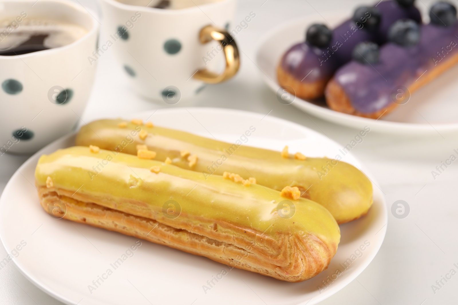 Photo of Tasty glazed eclairs on white table, closeup