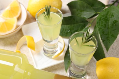 Photo of Tasty limoncello liqueur, lemons and green leaves on table, closeup