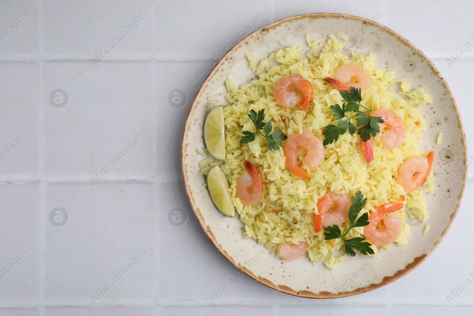 Photo of Delicious risotto with shrimps, lime and parsley on white tiled table, top view. Space for text