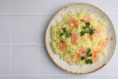 Delicious risotto with shrimps, lime and parsley on white tiled table, top view. Space for text