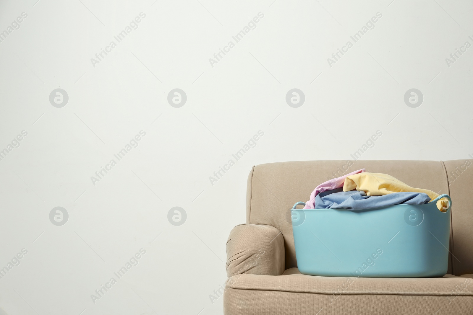 Photo of Laundry basket with dirty clothes on sofa at wall, space for text