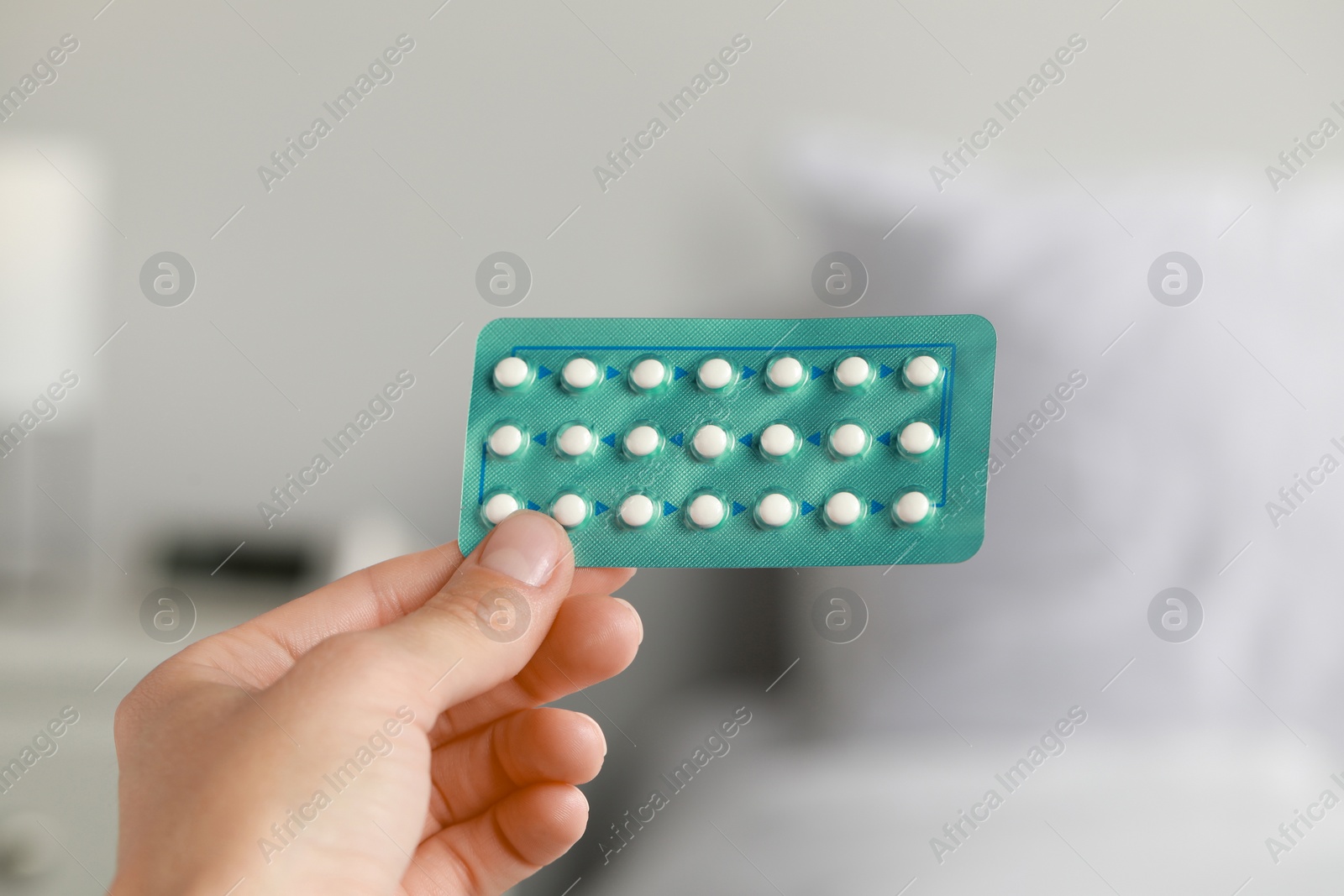 Photo of Woman holding blister of oral contraception pills against blurred background, closeup