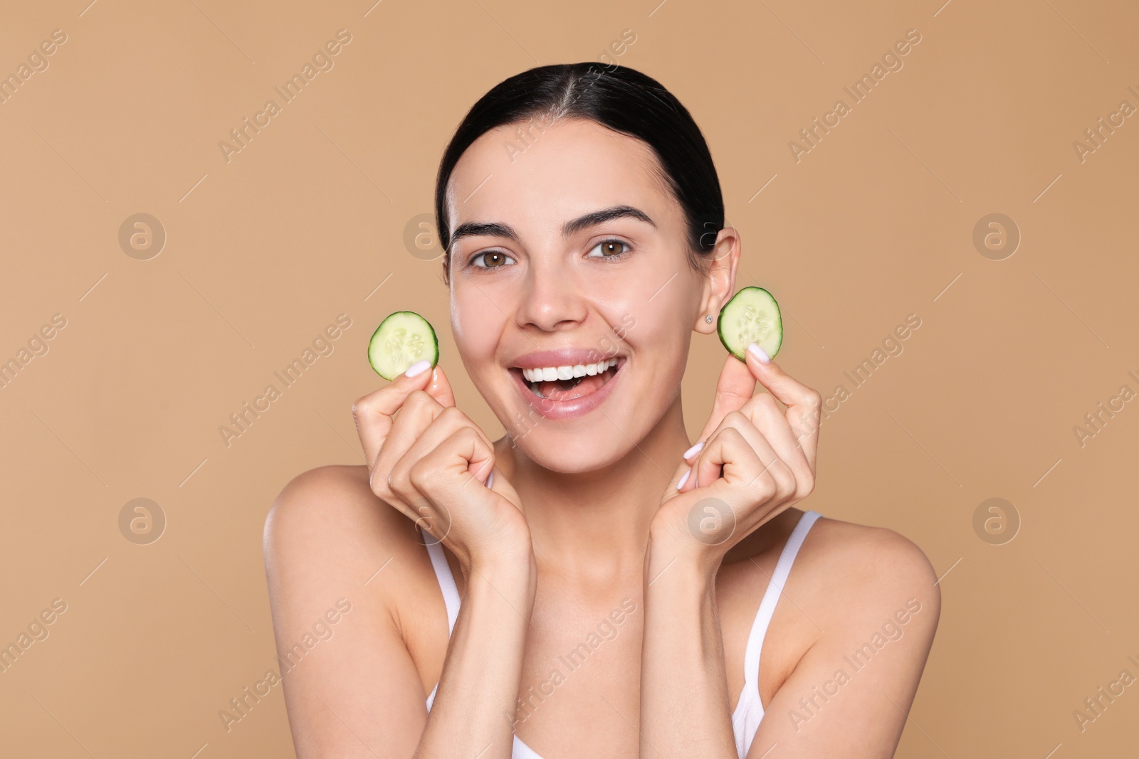 Photo of Beautiful young woman with slices of cucumber on beige background