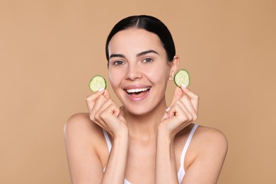 Photo of Beautiful young woman with slices of cucumber on beige background