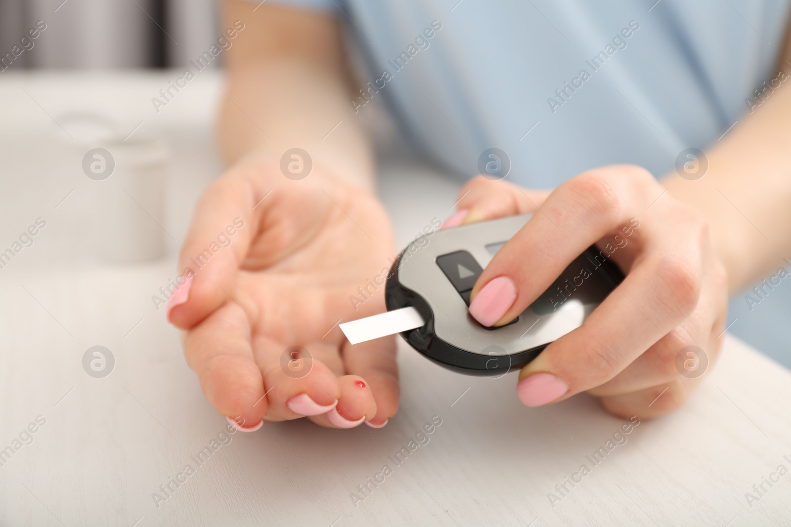 Photo of Diabetes. Woman checking blood sugar level with glucometer at wooden table, closeup