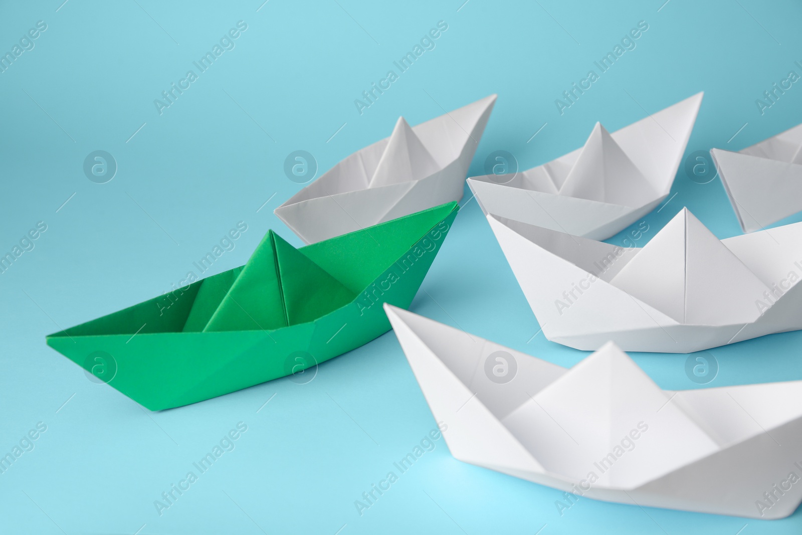 Photo of Group of paper boats following green one on light blue background. Leadership concept