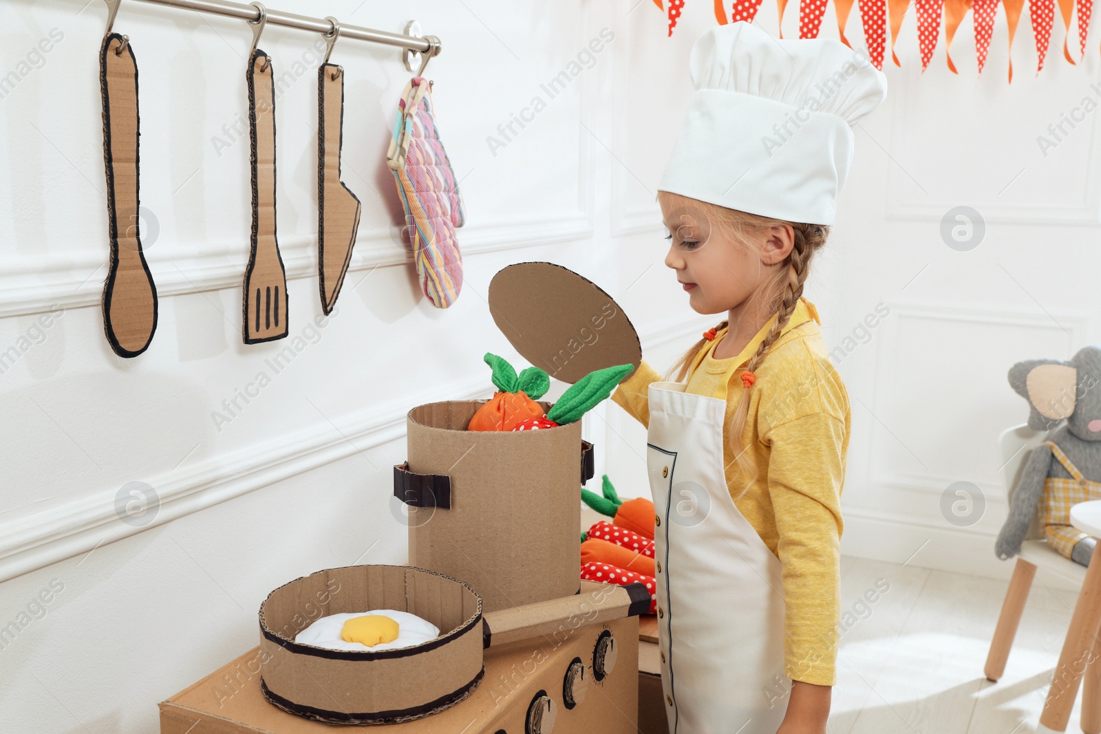 Photo of Little girl playing with toy cardboard kitchen at home