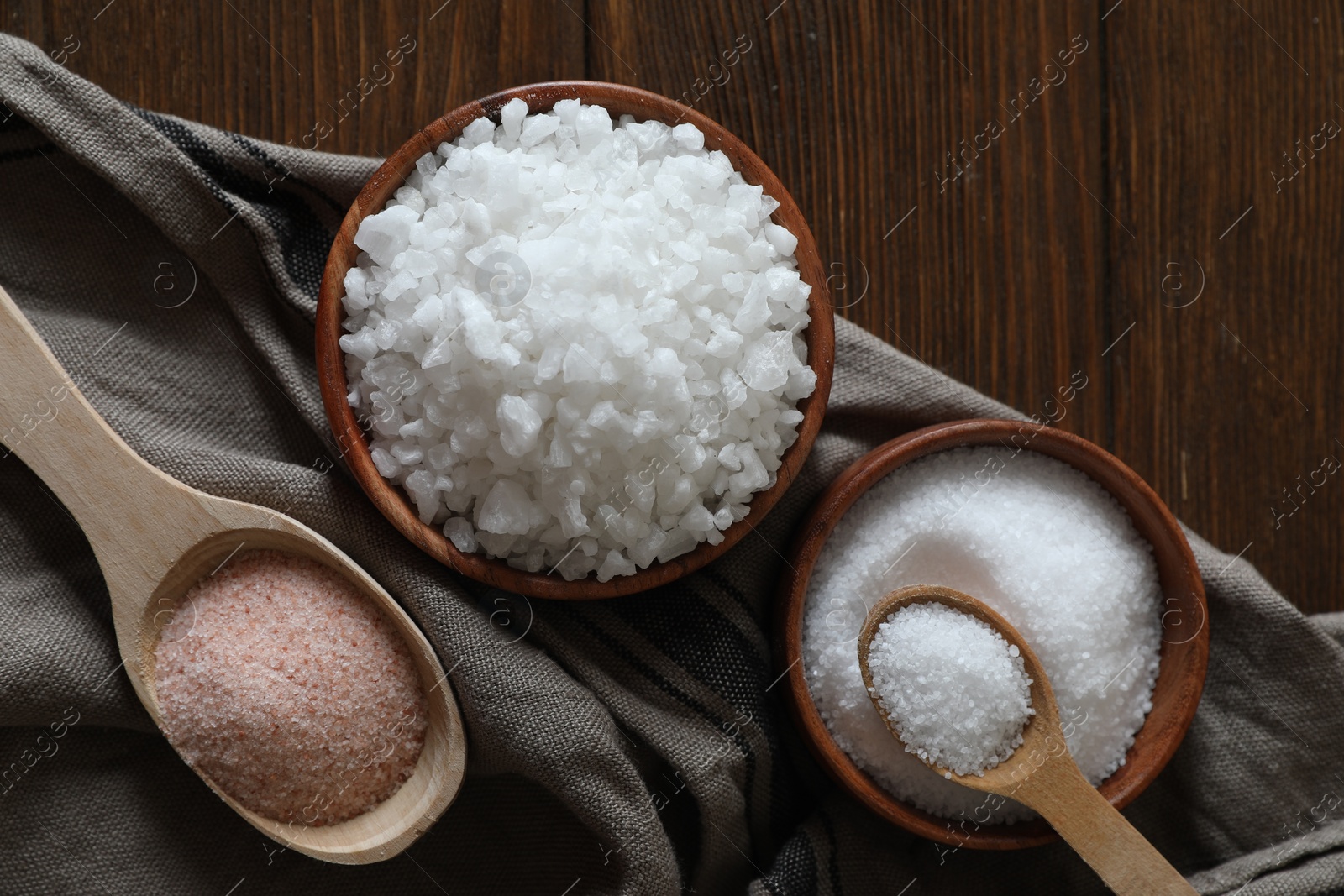 Photo of Different types of organic salt on wooden table, flat lay