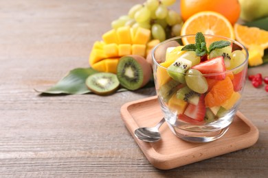 Photo of Delicious fresh fruit salad in dish on wooden table, space for text