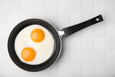 Tasty fried eggs in pan on white table, top view