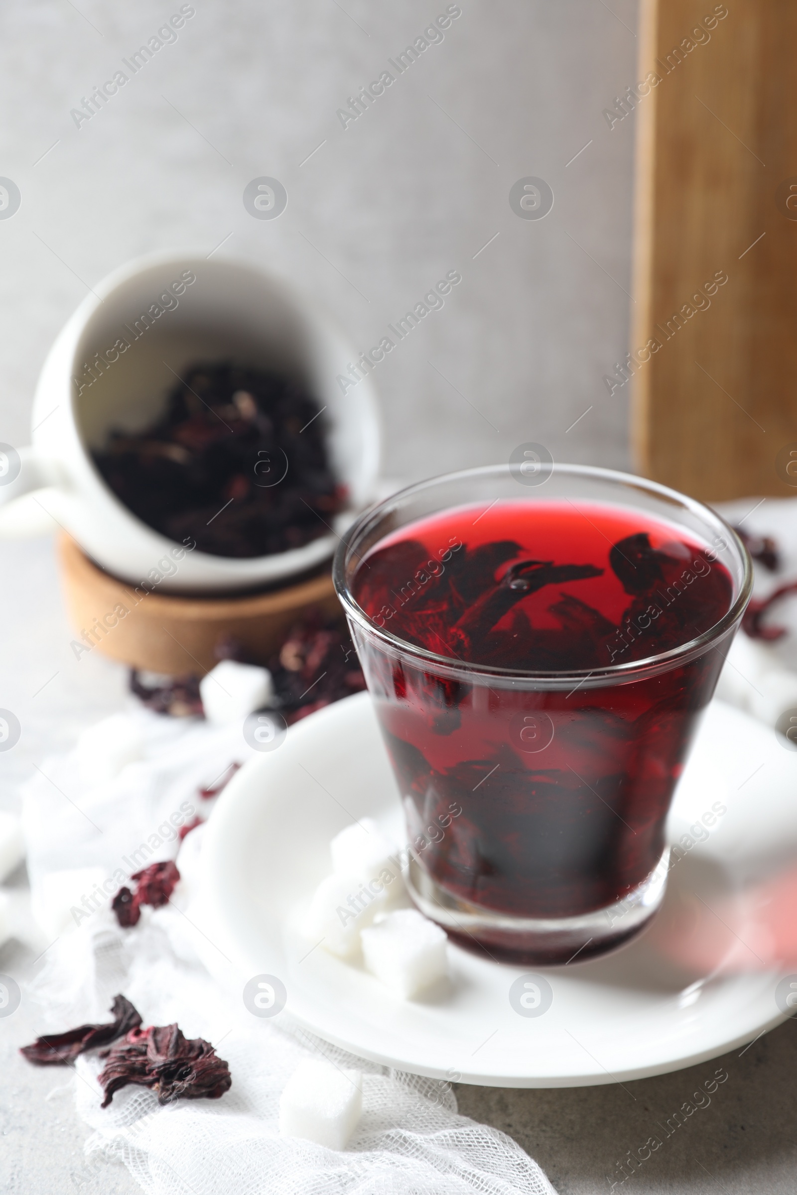 Photo of Aromatic hibiscus tea in glass, dried roselle calyces and sugar cubes on light table