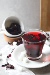 Photo of Aromatic hibiscus tea in glass, dried roselle calyces and sugar cubes on light table