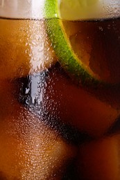 Glass of refreshing drink with sliced lime and ice cubes as background, closeup