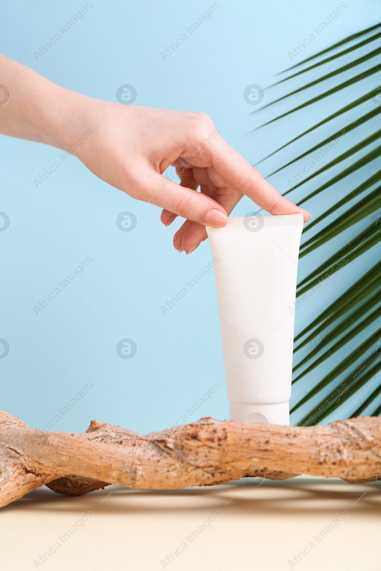 Photo of Woman with tube of cream and plant against light blue background, closeup