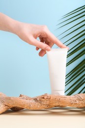 Woman with tube of cream and plant against light blue background, closeup