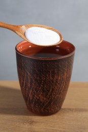 Spoon with baking soda over glass of water on wooden table