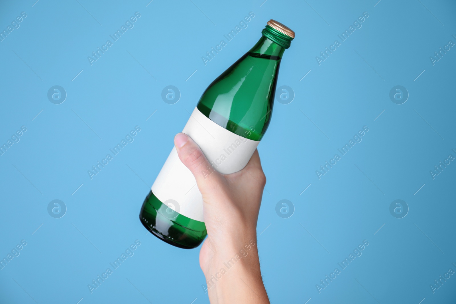 Photo of Woman holding glass bottle with soda water on light blue background, closeup