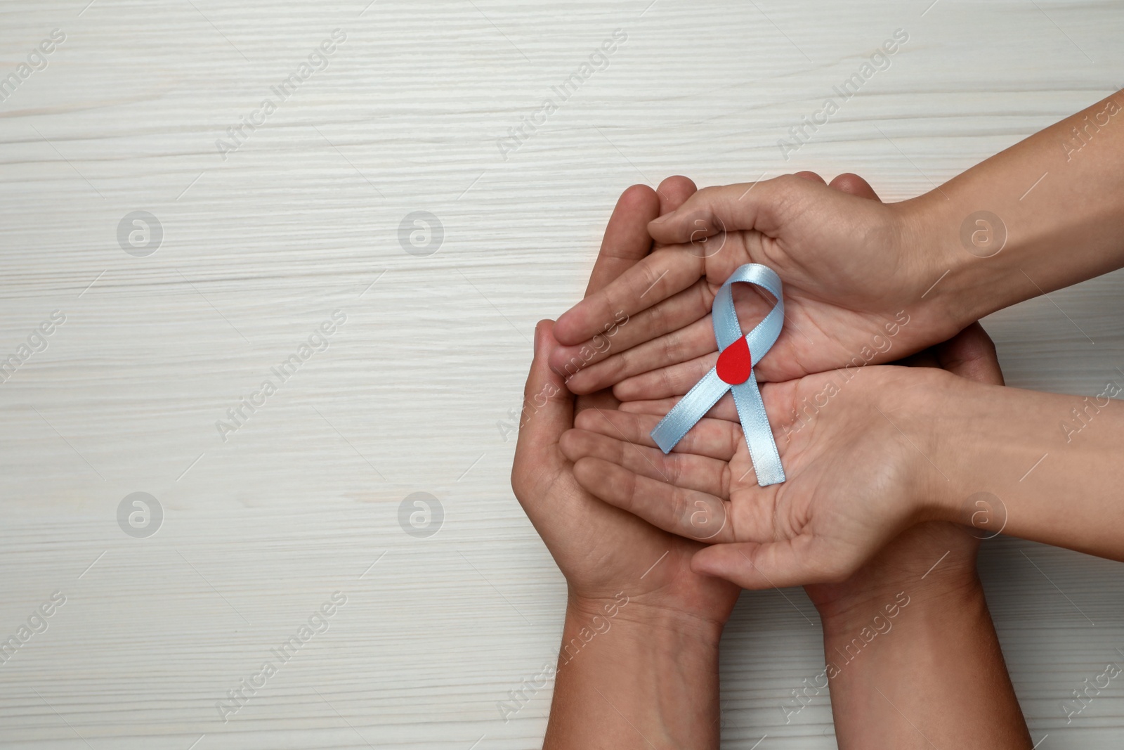Photo of People holding light blue ribbon with paper blood drop on white wooden background, top view and space for text. Diabetes awareness
