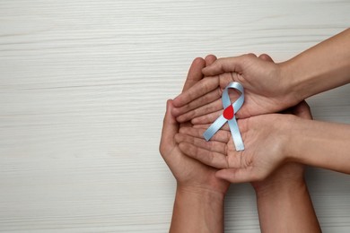 People holding light blue ribbon with paper blood drop on white wooden background, top view and space for text. Diabetes awareness
