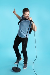 Photo of Young handsome man in casual clothes singing with microphone on color background