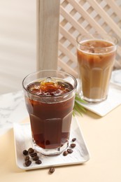 Photo of Refreshing iced coffee with milk in glasses and beans on beige table
