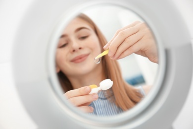 Photo of Mirror reflection of teenage girl taking contact lens from container