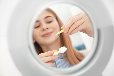 Mirror reflection of teenage girl taking contact lens from container