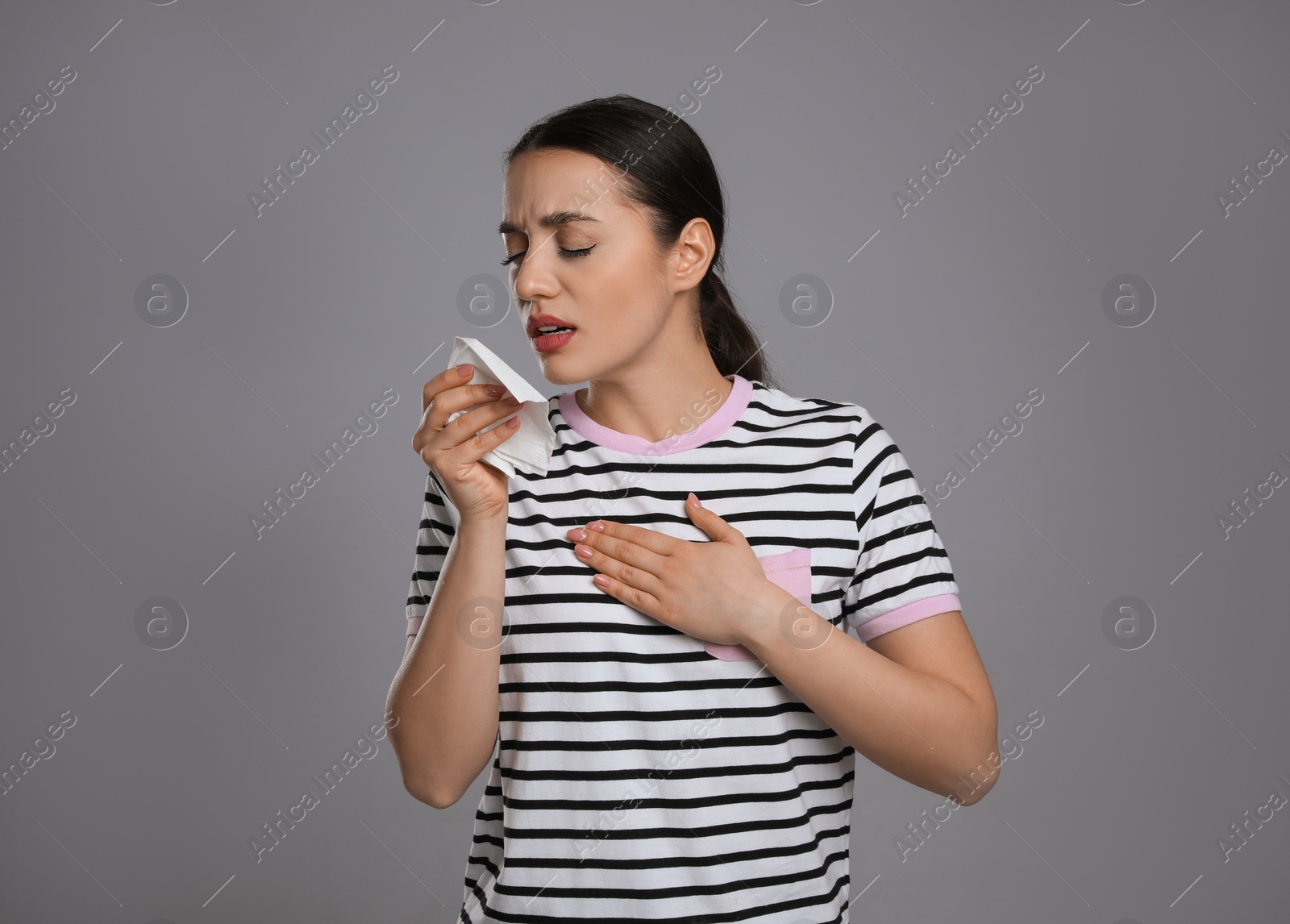 Photo of Young woman with tissue coughing on grey background. Cold symptoms